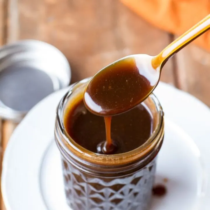 Spoon drizzling Guinness coffee salted caramel sauce into a glass jar.
