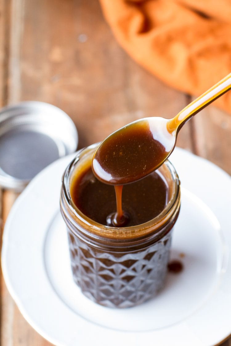 Spoon drizzling Guinness coffee salted caramel sauce into a glass jar.