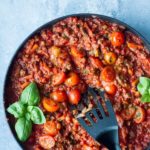 Bolognese sauce in a large skillet, garnished with fresh basil. Blue background.