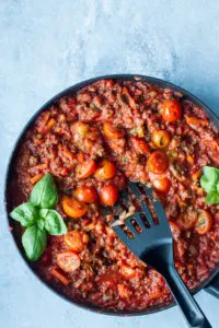 Bolognese sauce in a large skillet, garnished with fresh basil. Blue background.