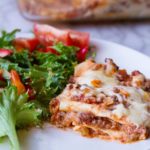 Lasagna and side salad on a white plate.
