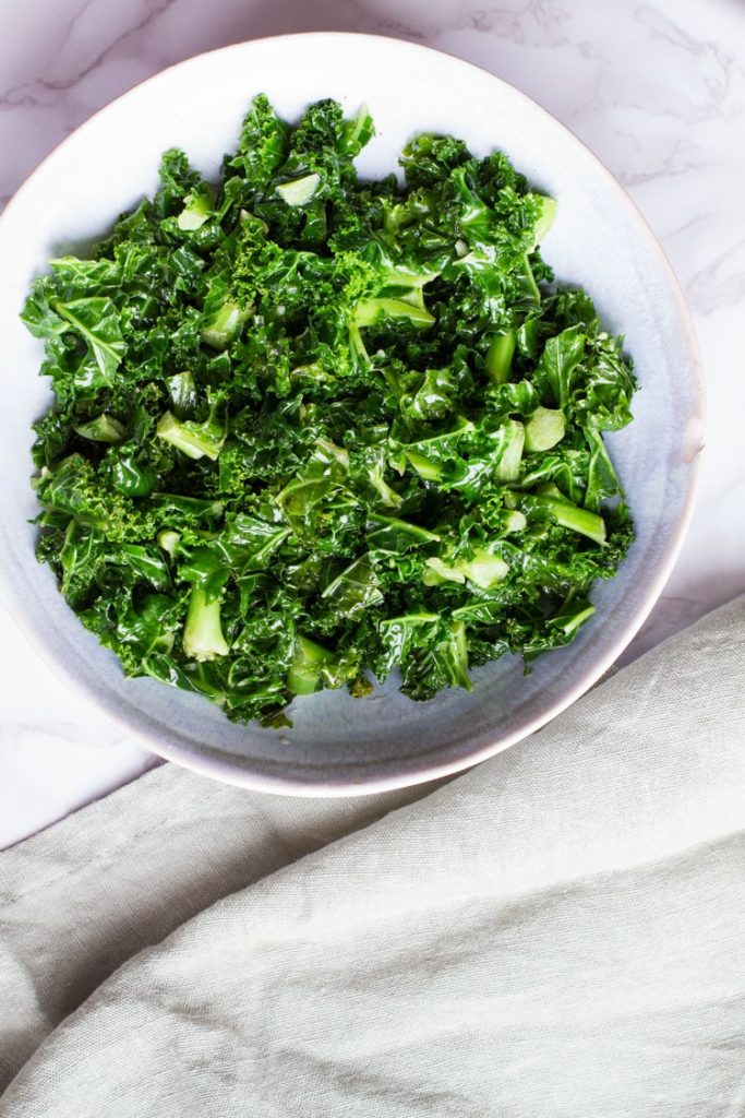 Big bowl of sauteed kale. Pastel green linen on the side.