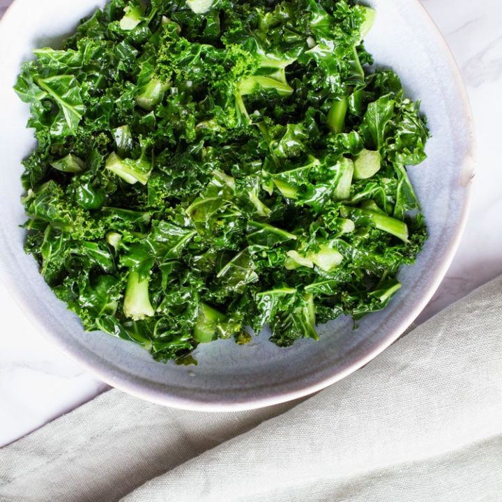 Big bowl of sauteed kale. Pastel green linen on the side.