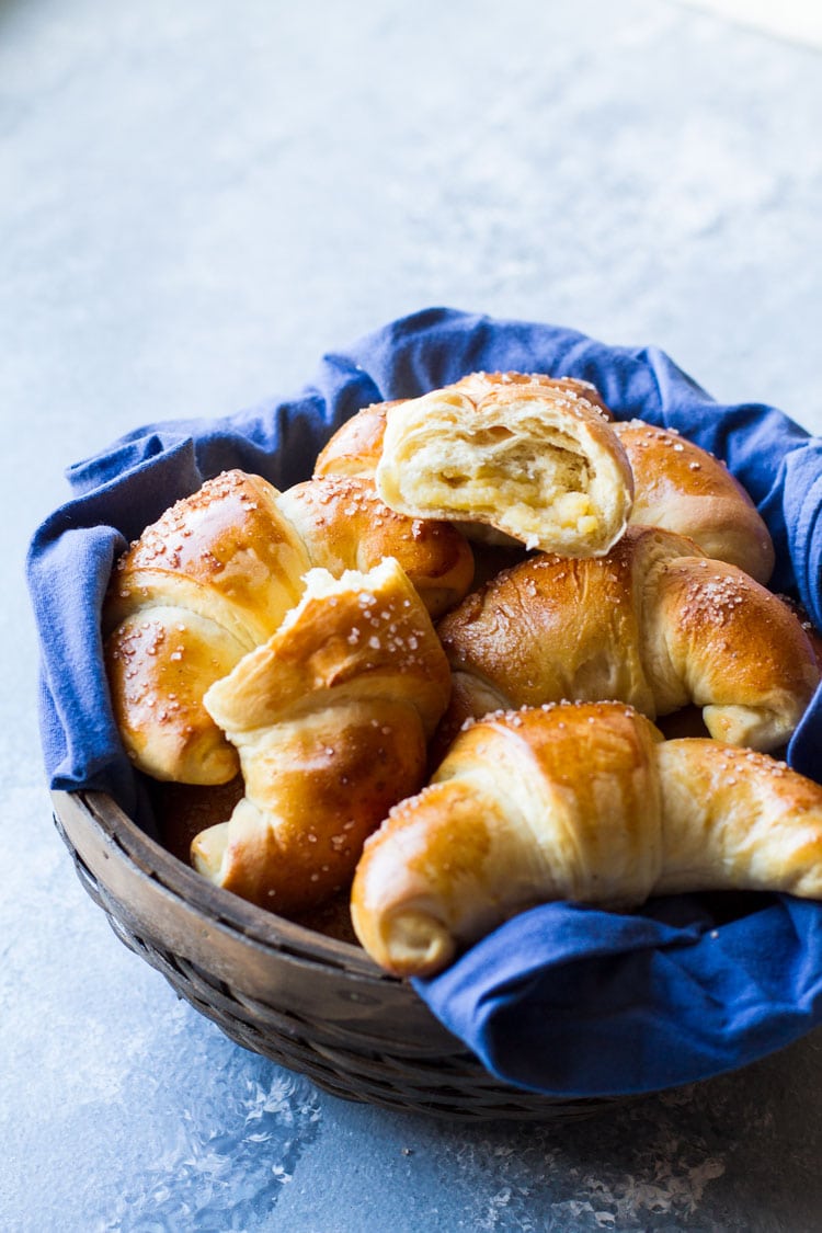 Wooden basket with blue linen and crescent rolls, one open.