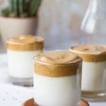 Glass with milk, topped with whipped coffee, on top of a terracotta plate.