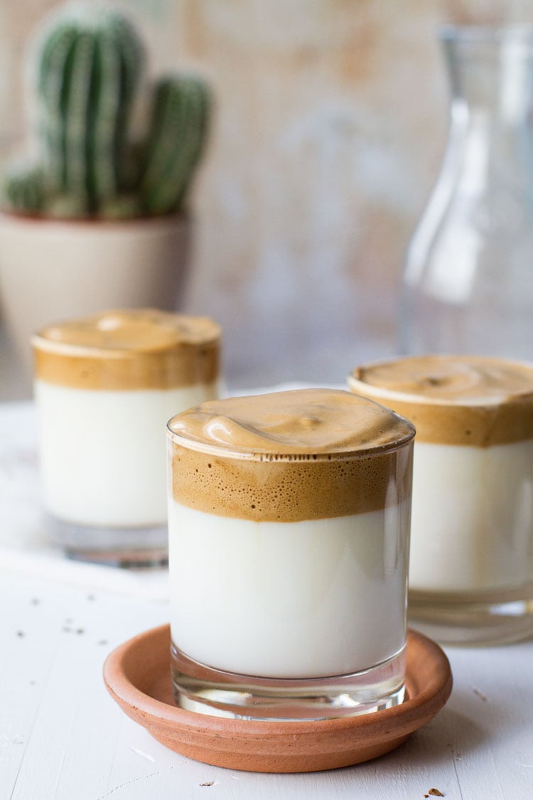 Glass with milk, topped with whipped coffee, on top of a terracotta plate.