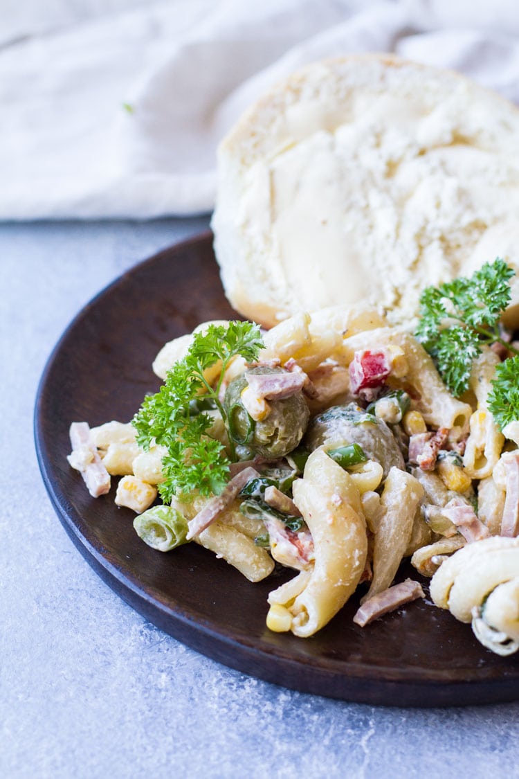 One serving of creamy pasta salad on a wooden plate with bread.