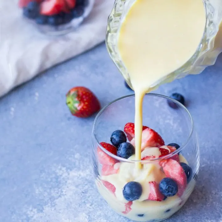 Pouring custard sauce over fresh berries in a glass.