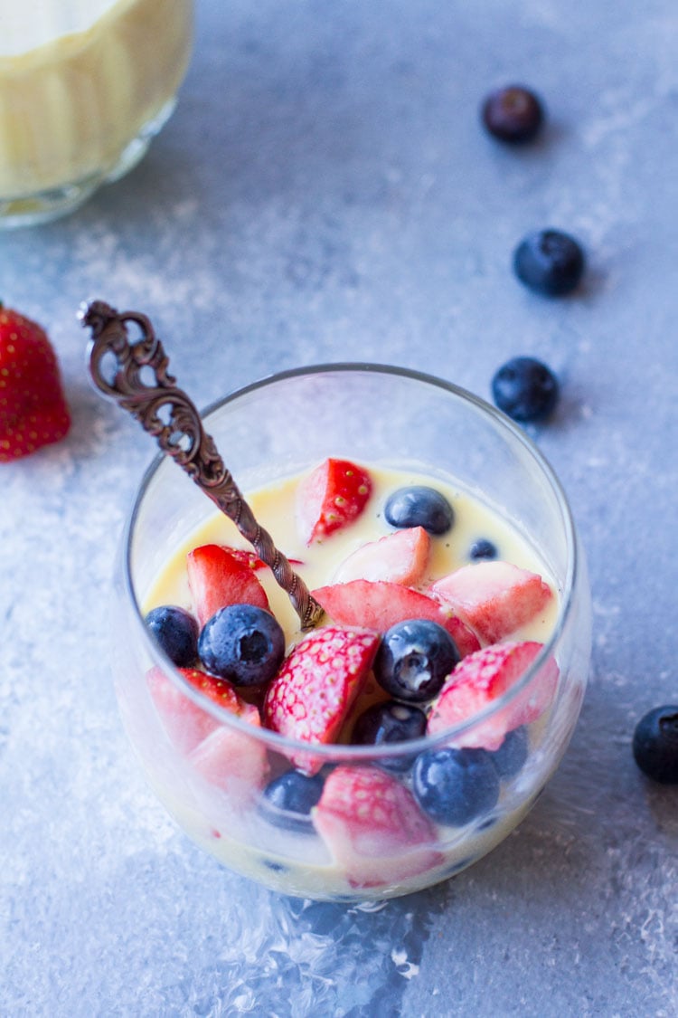 Glass with vintage spoon, fresh berries and custard sauce. Blue background.