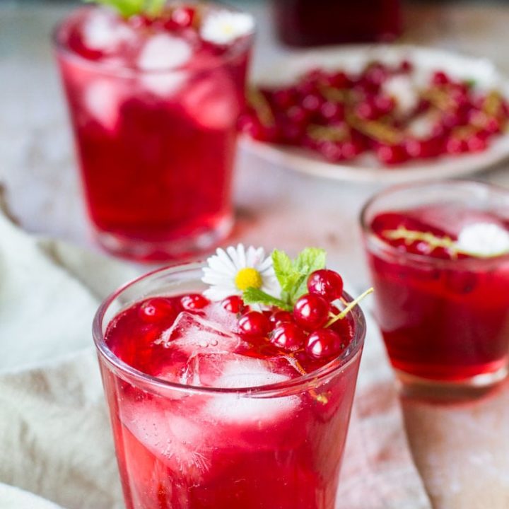 Three glasses with berry cordial, garnished with mint leaves and red currants.