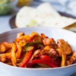 Chicken fajitas in a blue bowl, blue background.