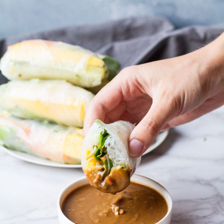 Hand holding a sliced open summer roll dipped in peanut sauce.