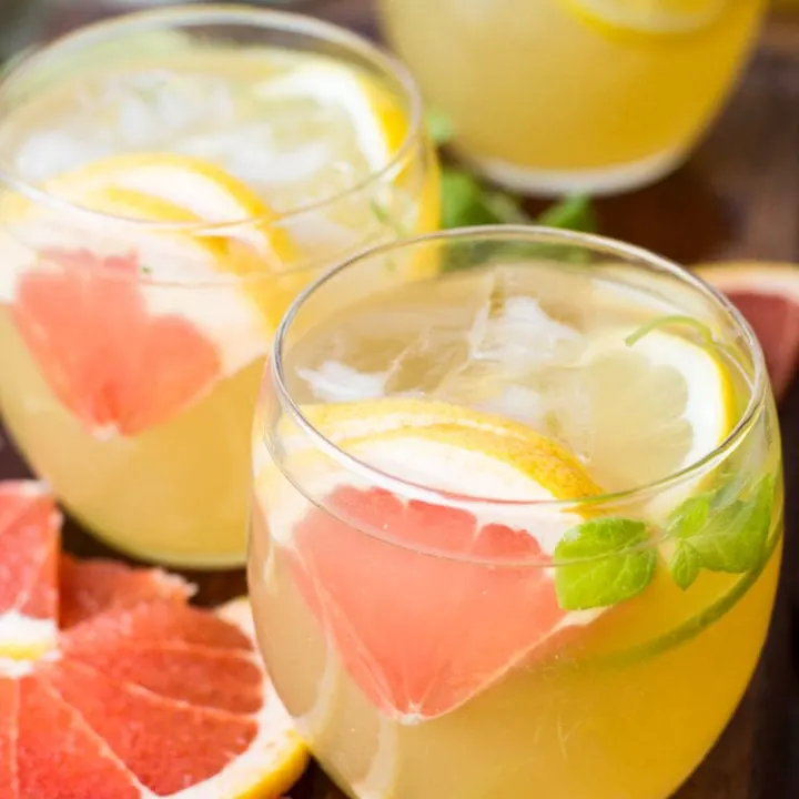 Round glasses with a yellow drink, sliced grapefruit and ice cubes.
