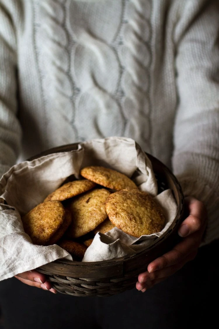A person in a white woollen sweater, holding a basket of cookies.