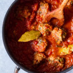 Close-up of a casserole with meatballs in tomato sauce and bay leaves.