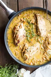 Four chicken breast in mustard cream sauce, garnished with thyme. Flat-lay.