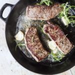 3 striploin steaks in a cast iron skillet with rosemary and garlic.