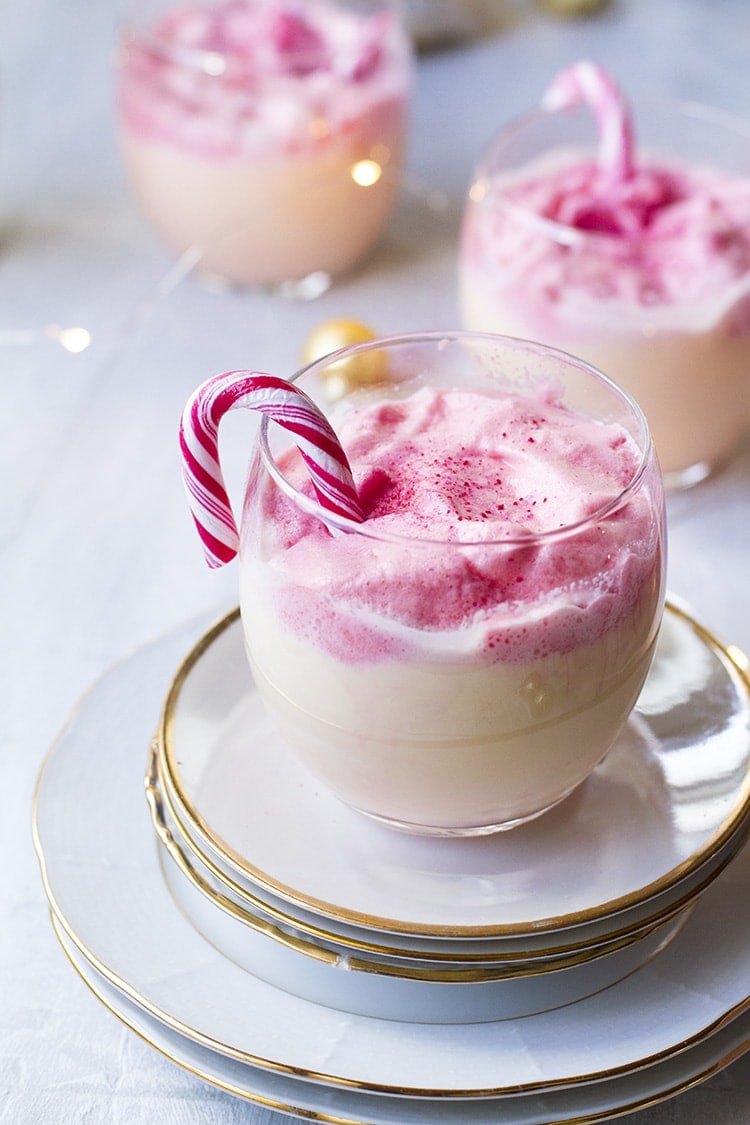 Round glass with eggnog and fluffy pink dalgona, garnished with candy cane.