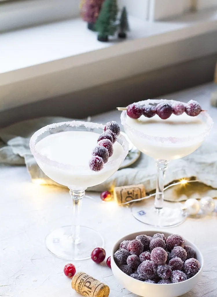 Two coupé glass with a white cocktail and sugar cranberries garnish.