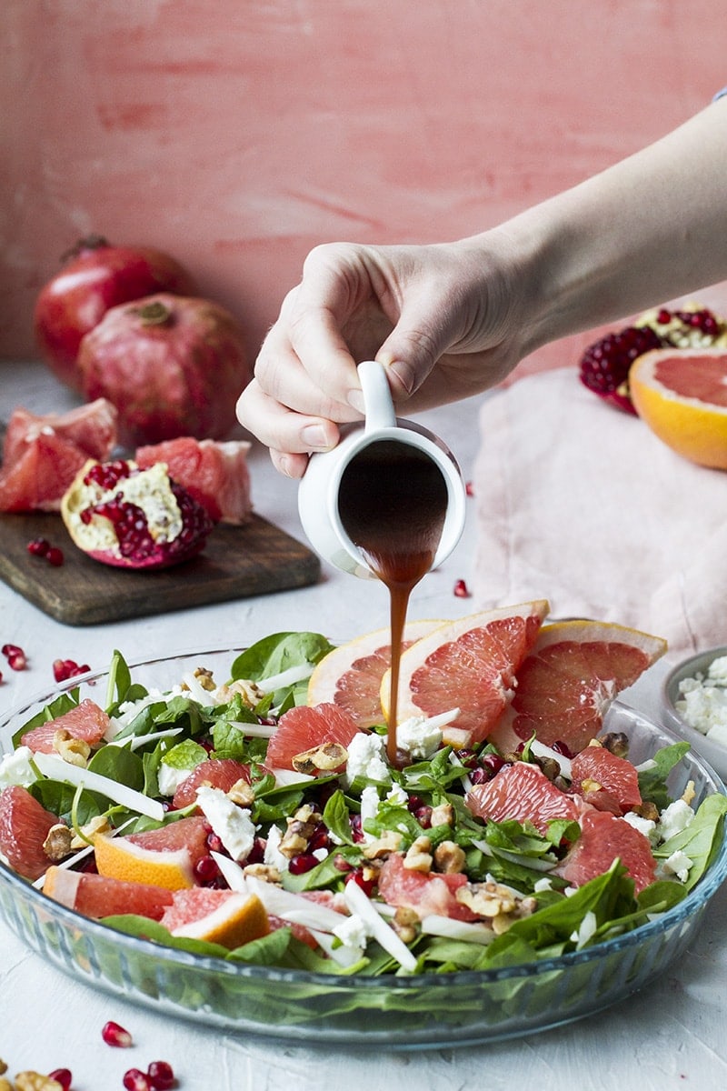 Hand pouring pomegranate vinaigrette over a grapefruit salad in a shallow pan.