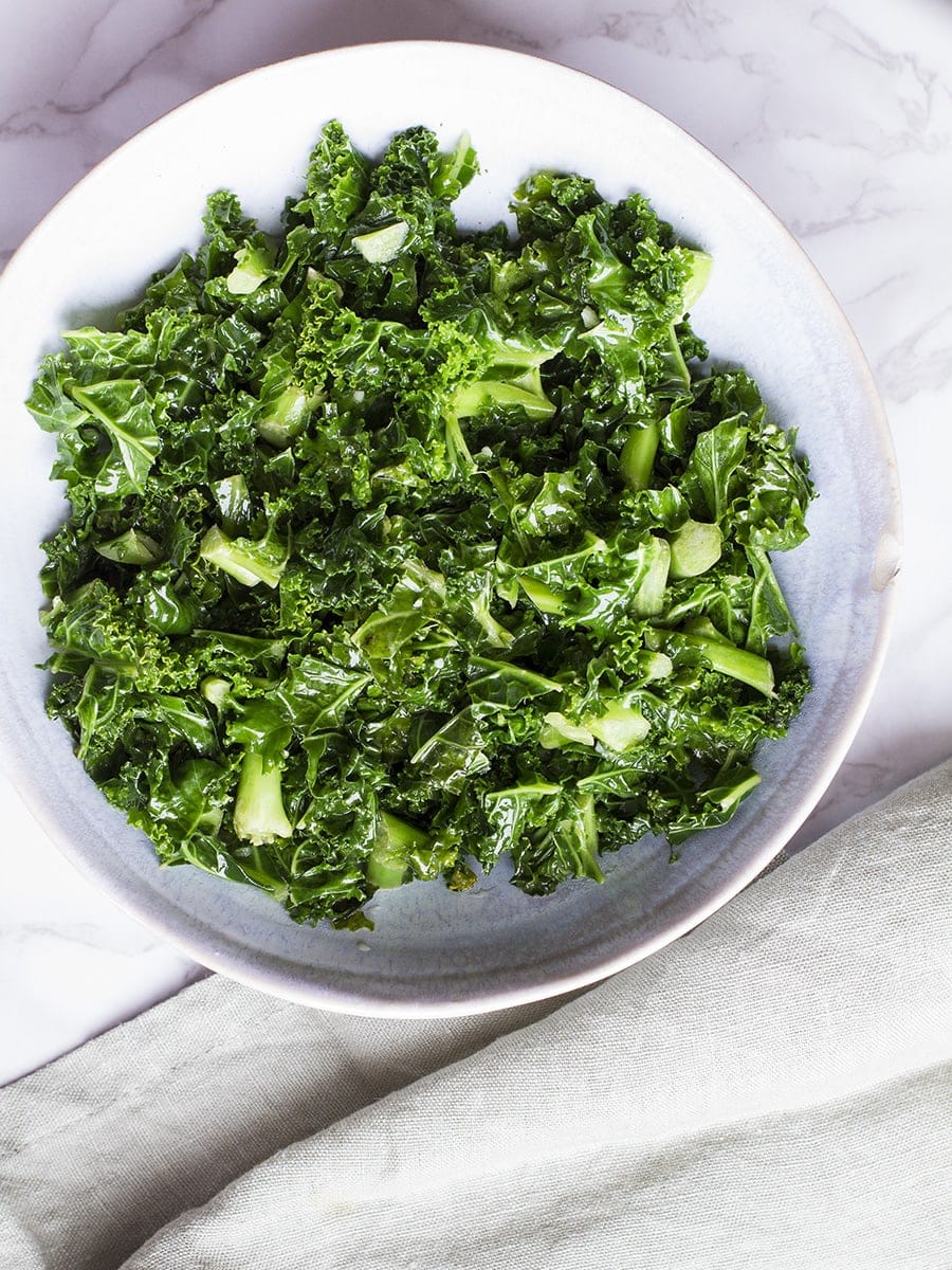 Big bowl of sauteed kale. Pastel pale green linen on the side.