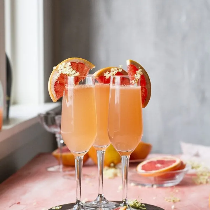Three grapefruit mimosas in champagne flutes. Pink table.