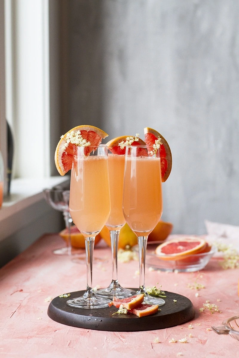 Three grapefruit mimosas in champagne flutes. Pink table.