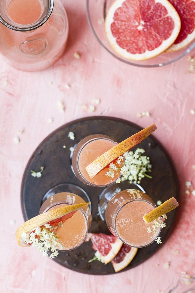 Three champagne flutes seen from above, garnished with grapefruit slices and elderflower.
