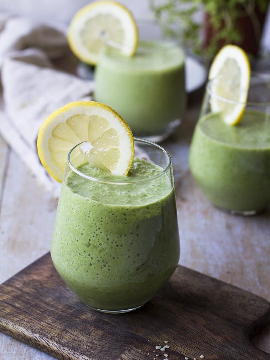 Wine glass with green smoothie and a lemon wedge.