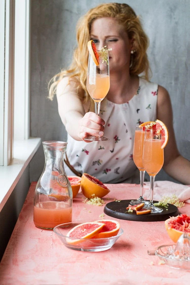 Girl holding up a champagne flute with grapefruit cocktail.