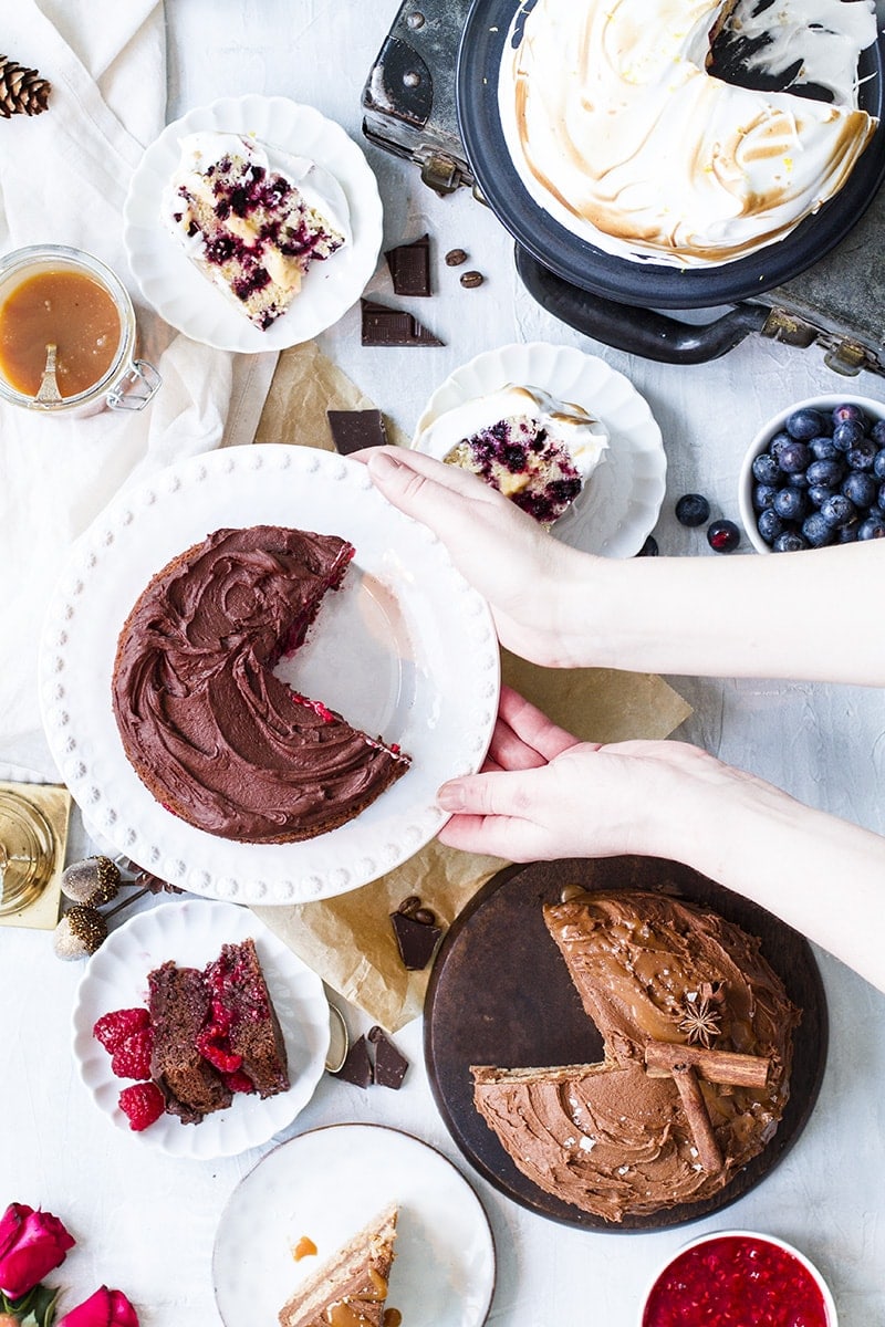 Flat-lay with multiple cakes and hands reaching for the cake stand in the middle.