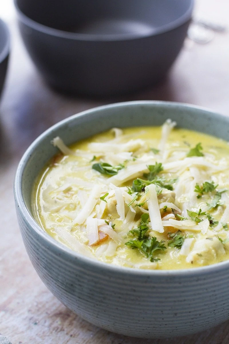 A green bowl with chicken soup that is garnished with shredded cheese and parsley.