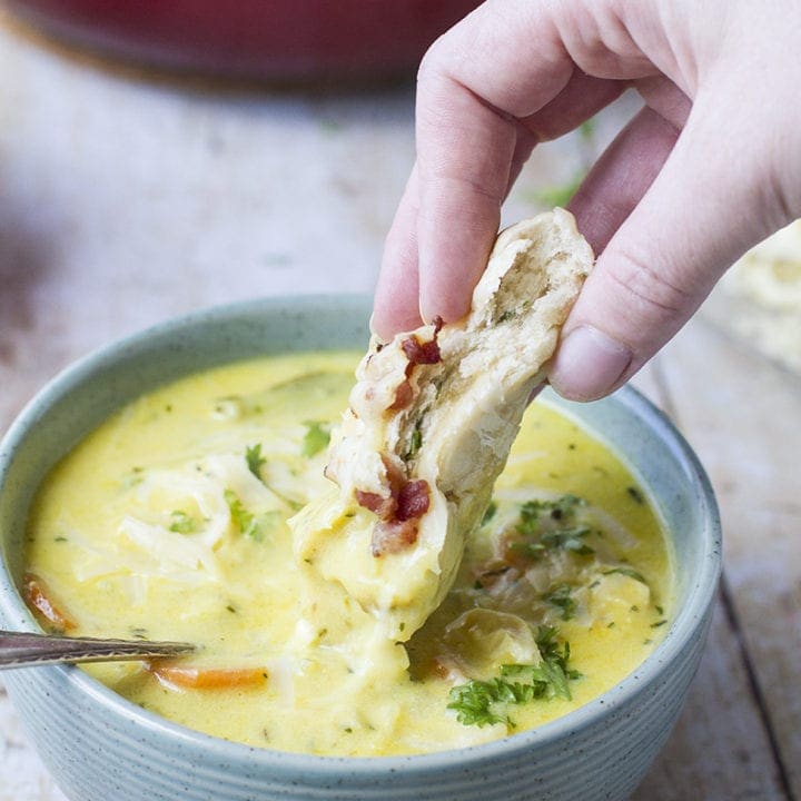 Hand dipping a bacon dinner roll in the soup.