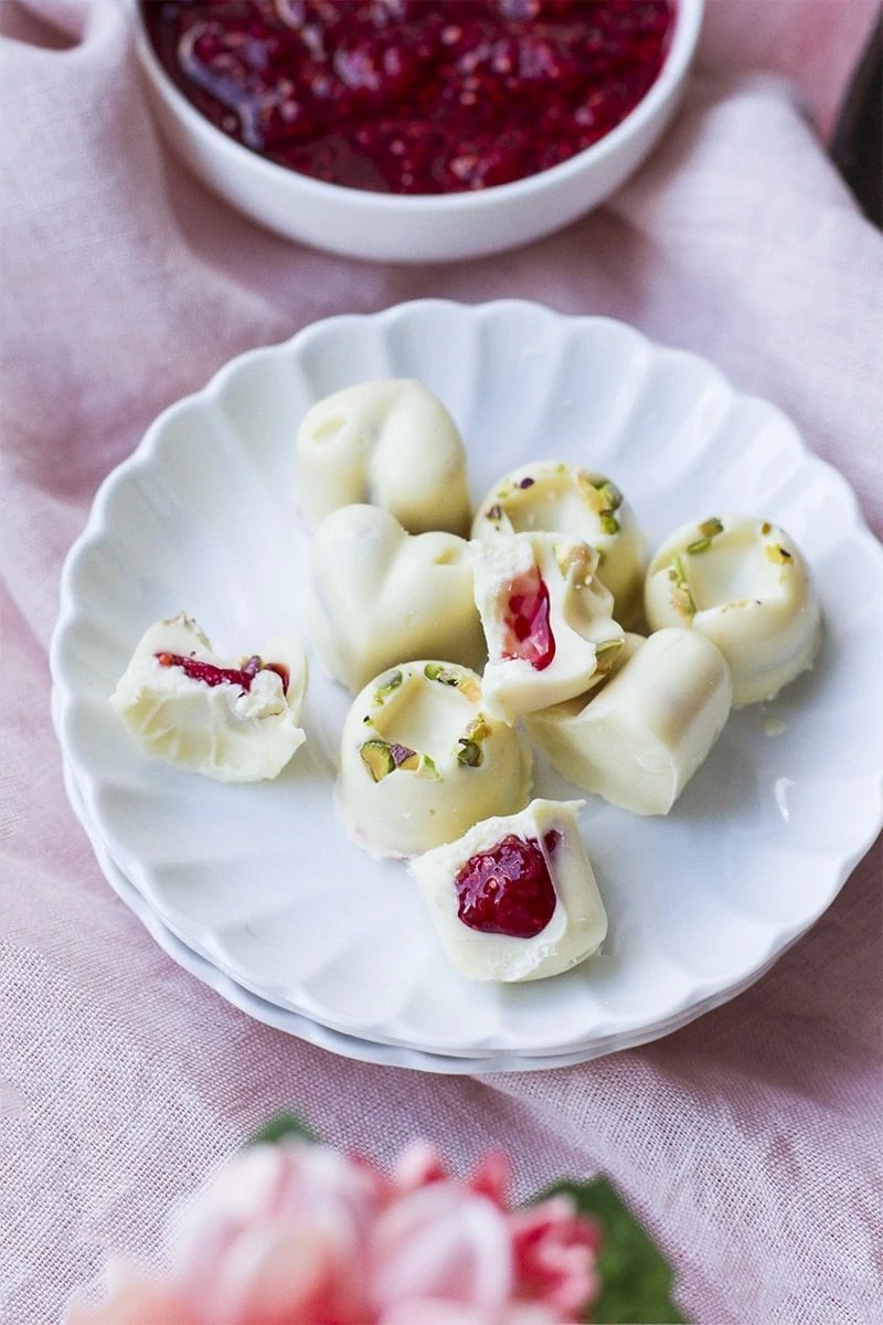 Raspberry filled white chocolates on a white plate. Pink background.