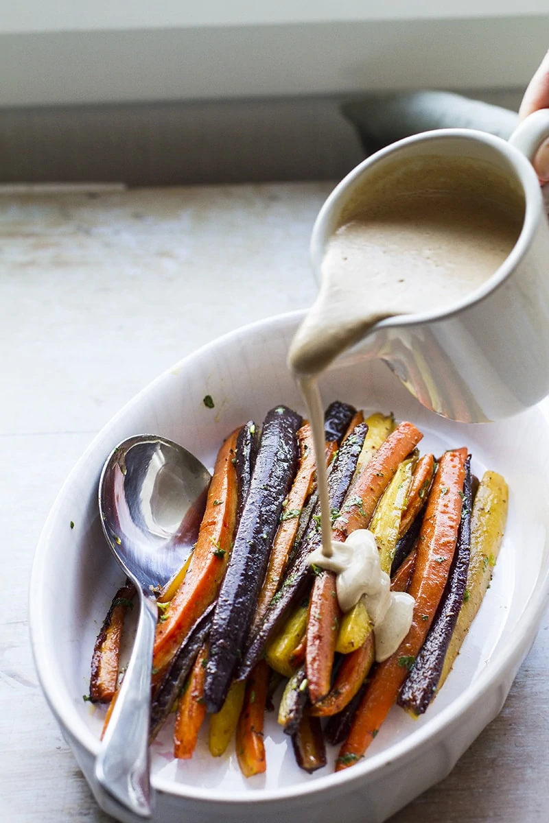 Pouring tahini sauce over the roasted carrots.