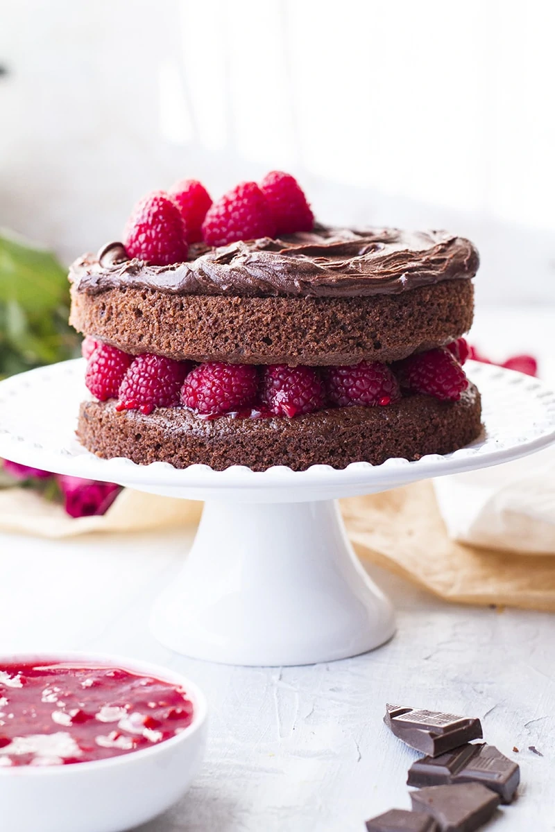 Chocolate cake with raspberry filling on a white cake stand.