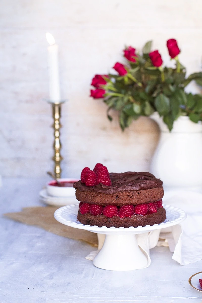 Chocolate raspberry cake on a cake stand, roses in the background.
