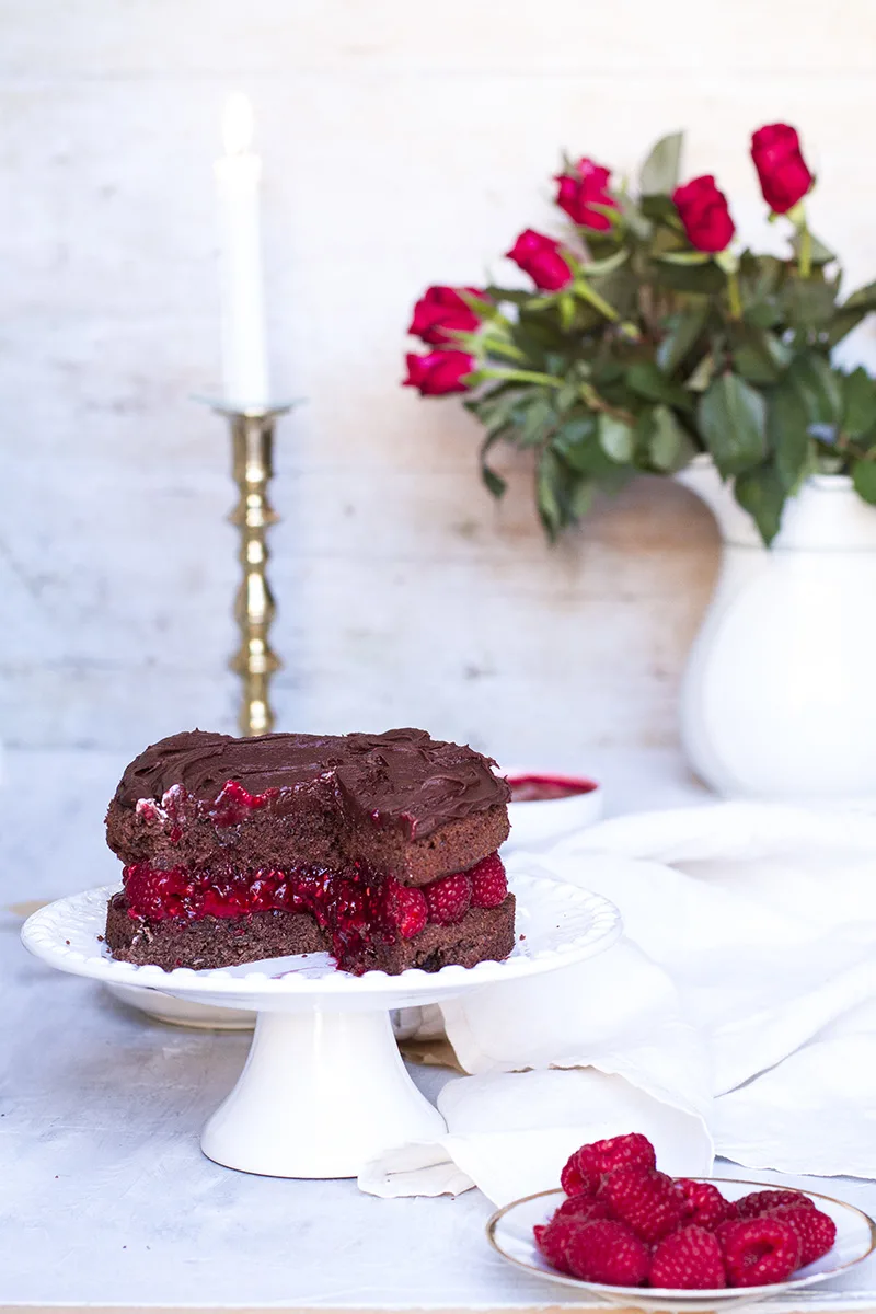 Cut open raspberry chocolate cake, roses in the background.