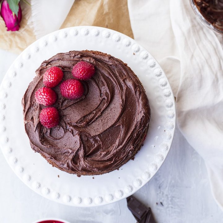 Raspberry chocolate cake on a white cake stand.
