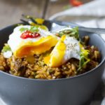 A dark grey bowl with fried rice and a runny poached egg on top.