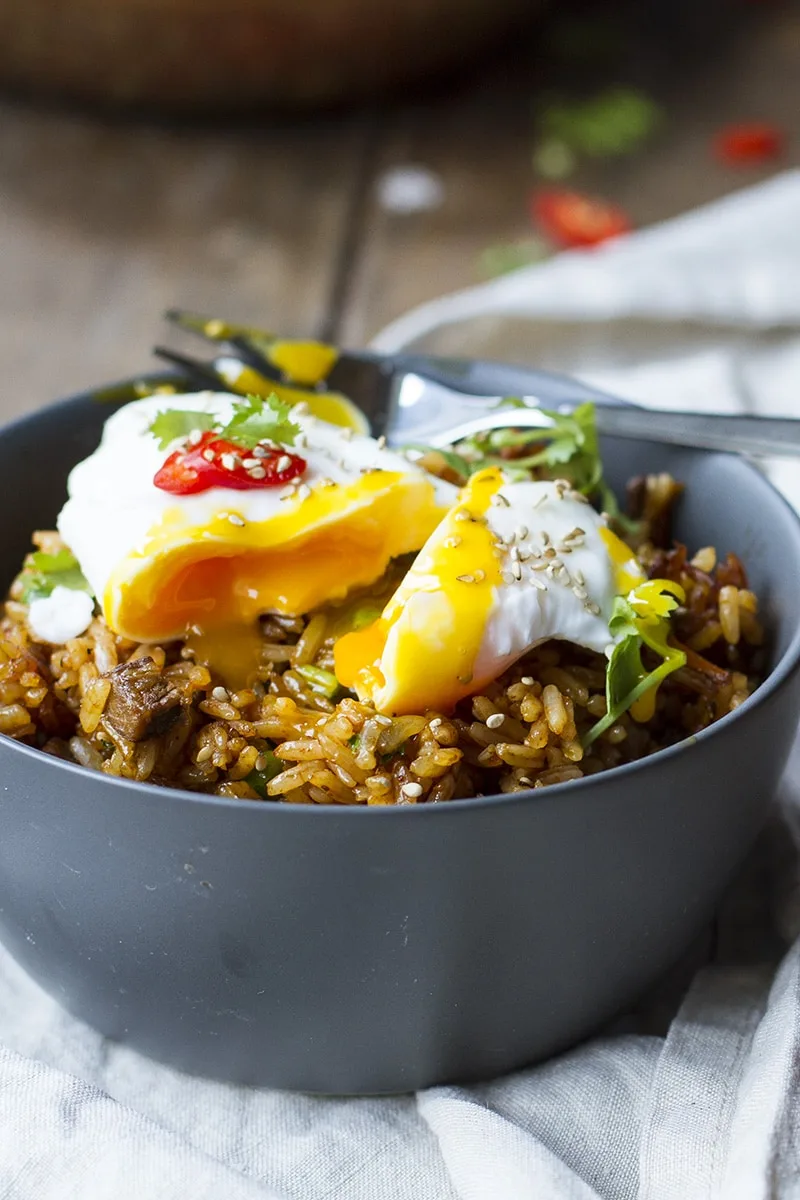 A dark grey bowl with fried rice and a runny poached egg on top.