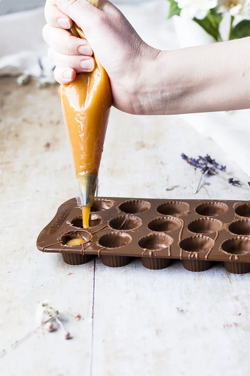 Piping bag piping caramel into chocolate moulds.