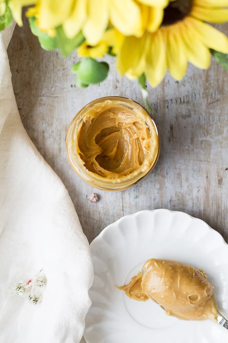 A vintage plate with a spoon of dulce de leche and a glass jar with the dulce de leche.