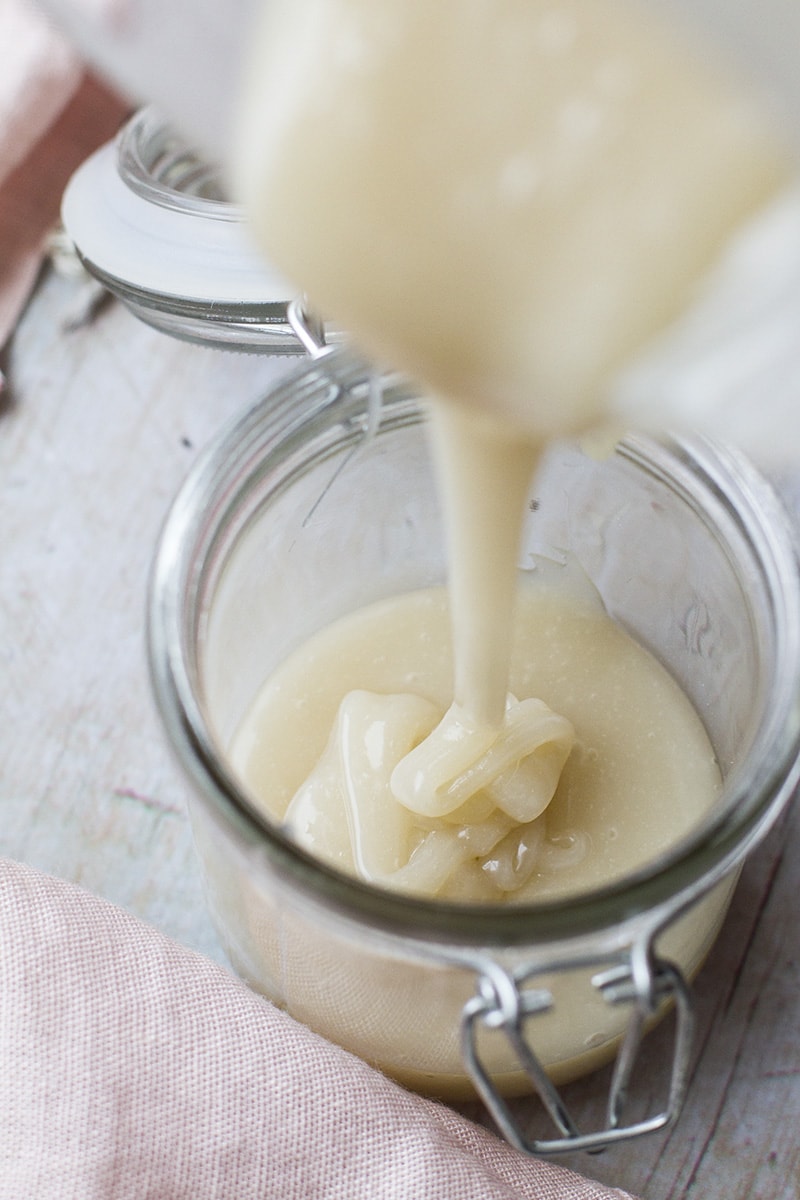 Pouring sweetened condensed coconut milk into a glass jar.