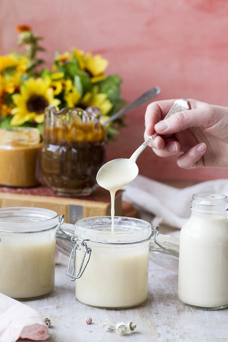 Spoon drizzling condensed milk into a jar. Four other containers around.