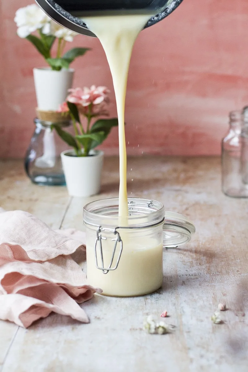 Pouring sweetened condensed milk into a glass jar.