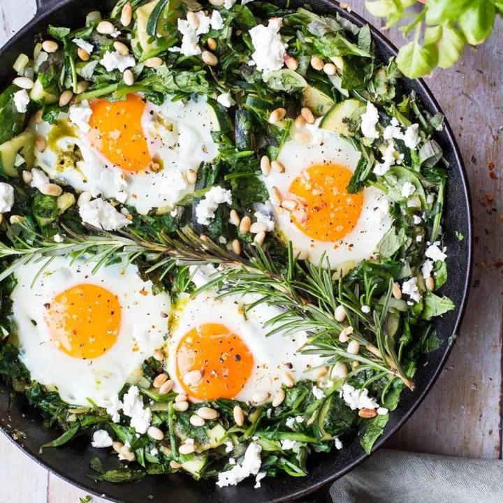 Cast iron skillet with green spinach bed and four sunny-side-up eggs.