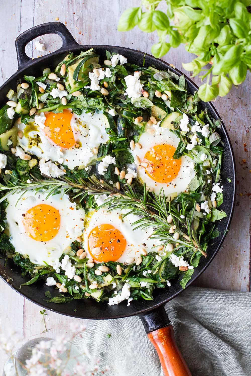 Cast iron skillet with green spinach bed and four sunny-side-up eggs.