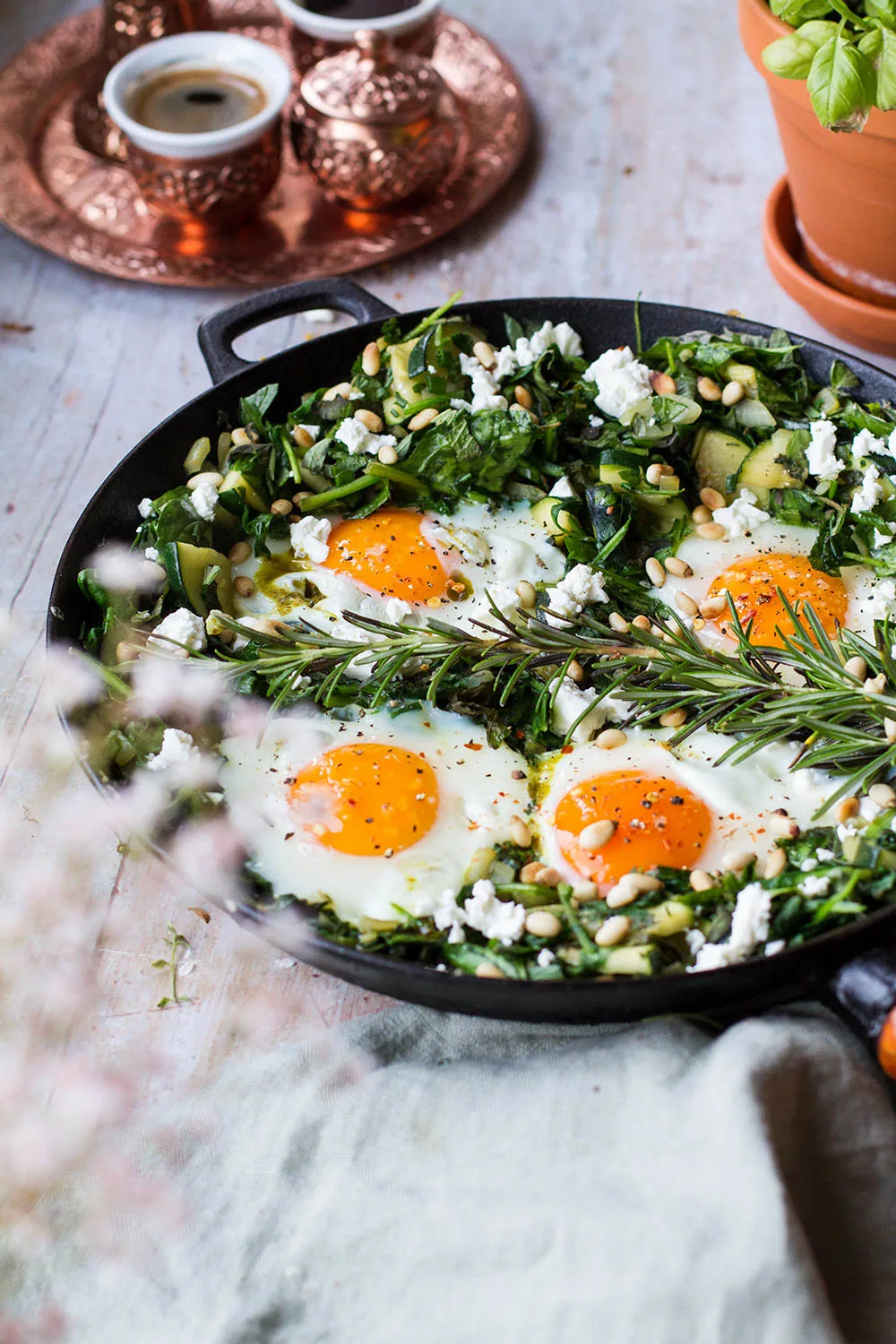 Four sunny-side-up eggs in a bed of greens in a skillet.