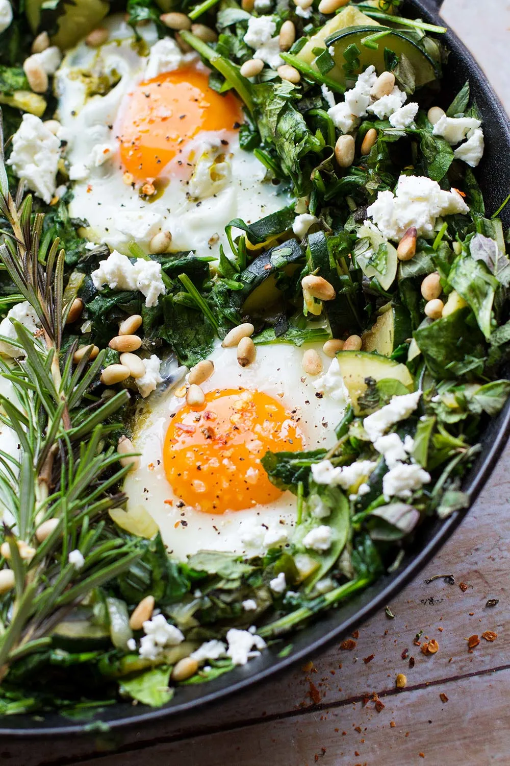 Close-up of the skillet showing two eggs, fresh rosemary and a bed of spinach.